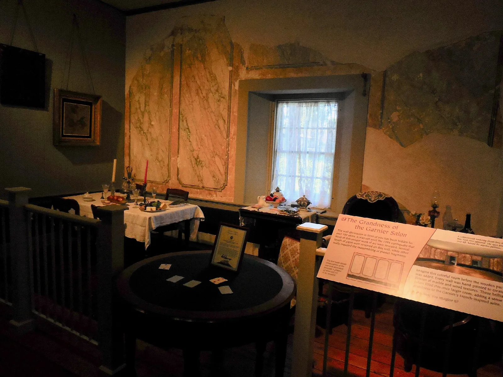 Dim room with a round table, framed pictures and a window behind a wooden railing