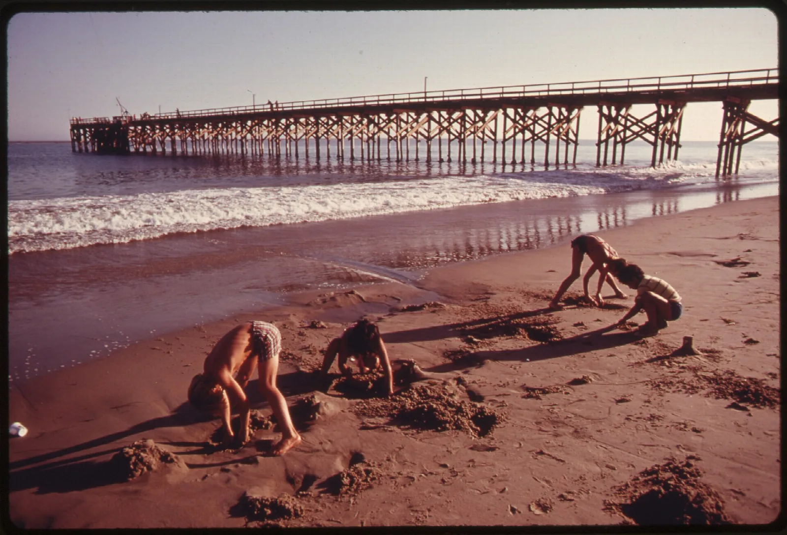 Faded vintage photo of children playing on the beach with the pier behind