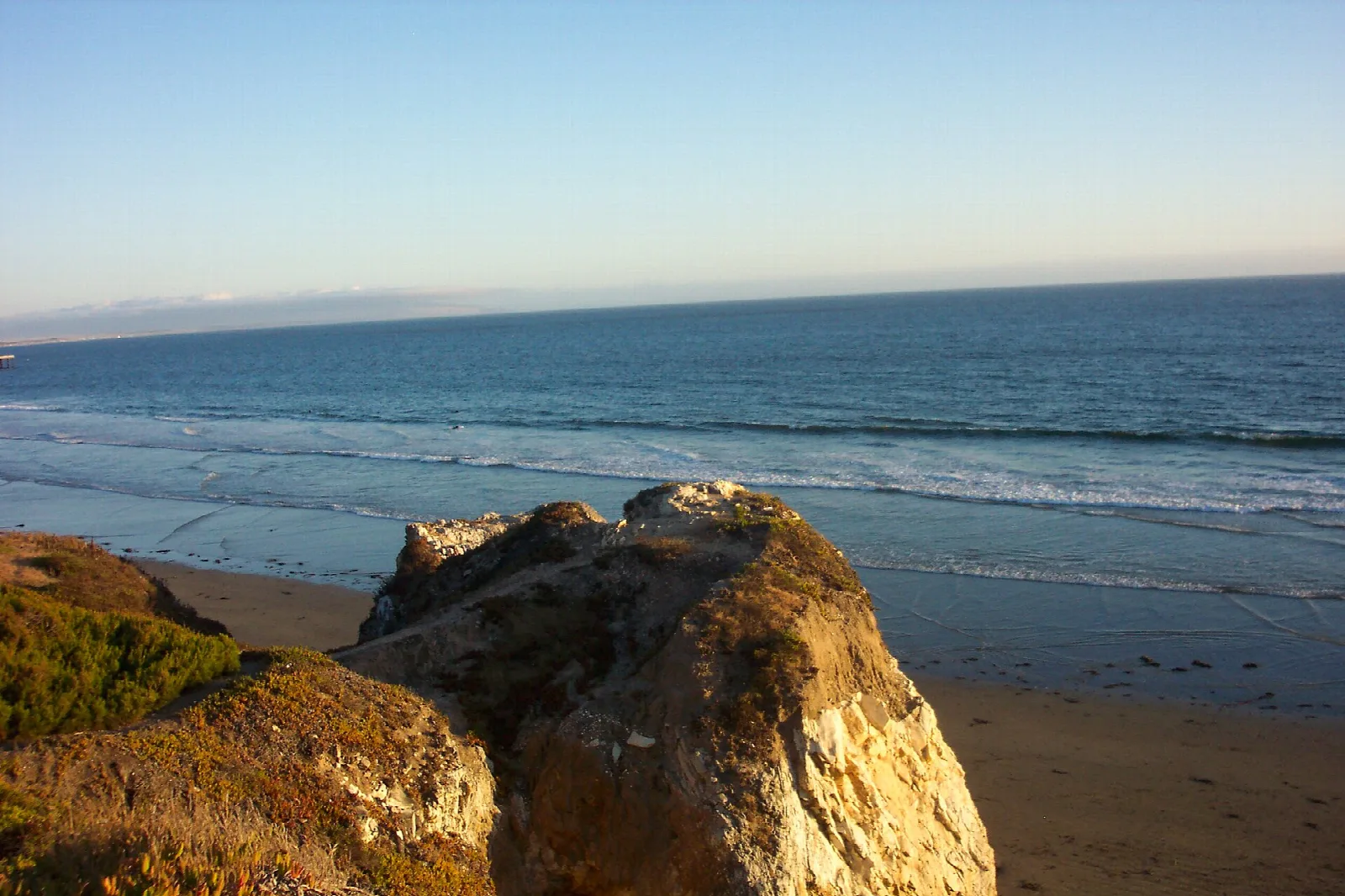 Golden rocks above a sandy beach and calm ocean at dusk