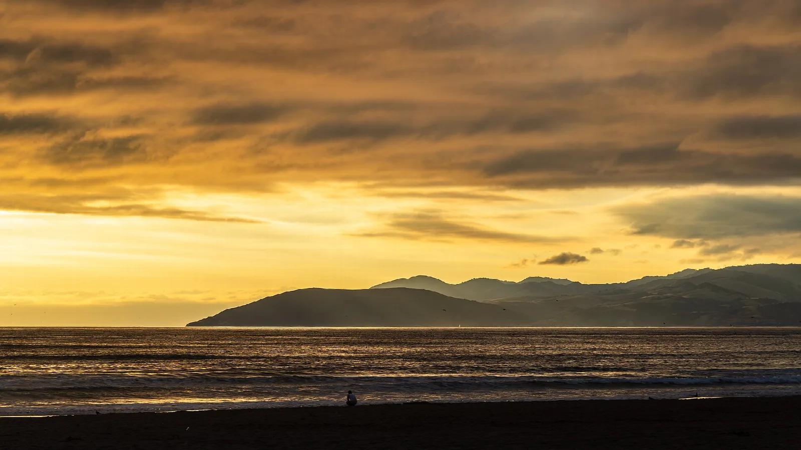 Orange clouds over the water with dark headland silhouette