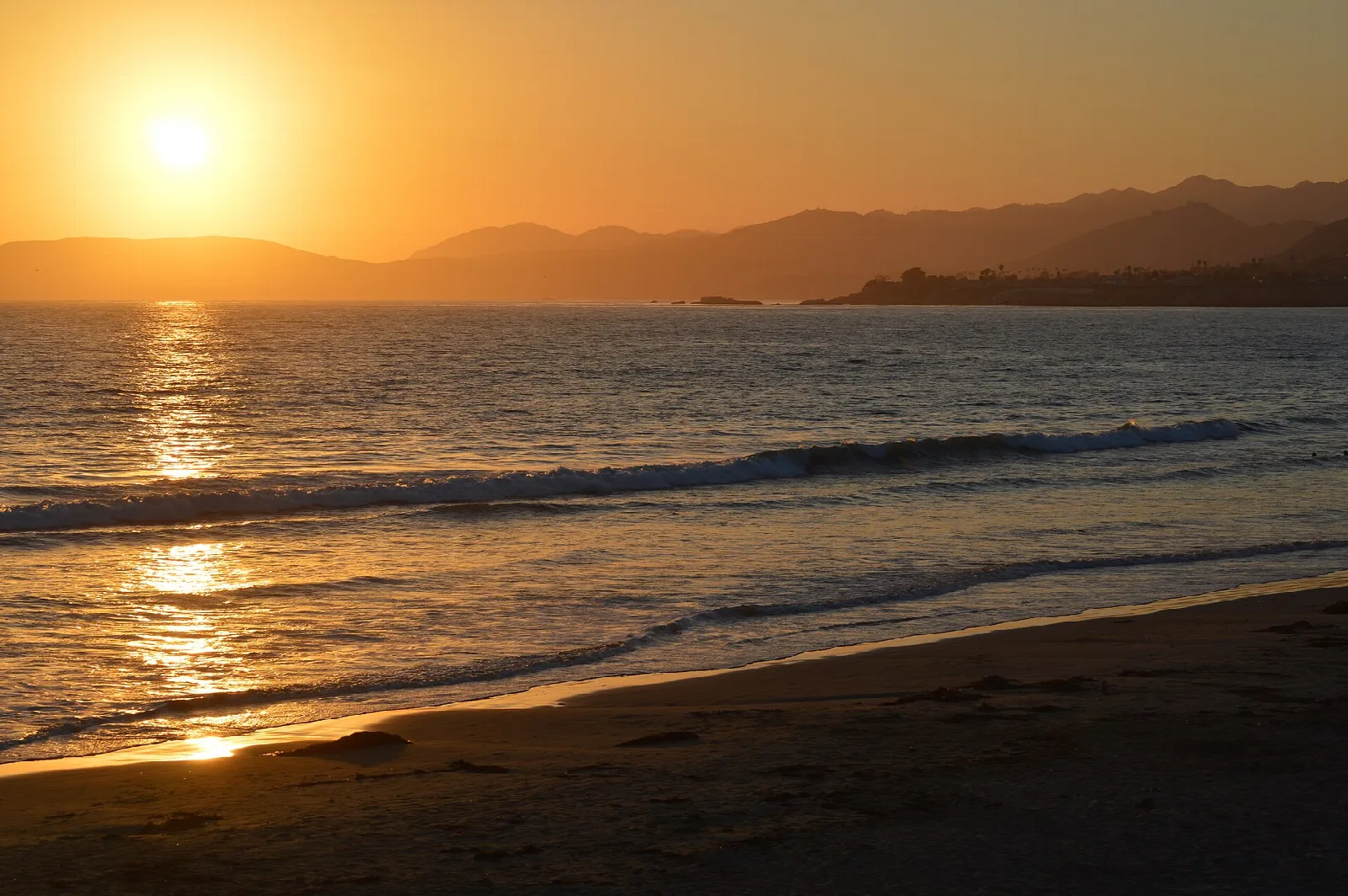 Sun setting over low hills and gentle waves on a beach