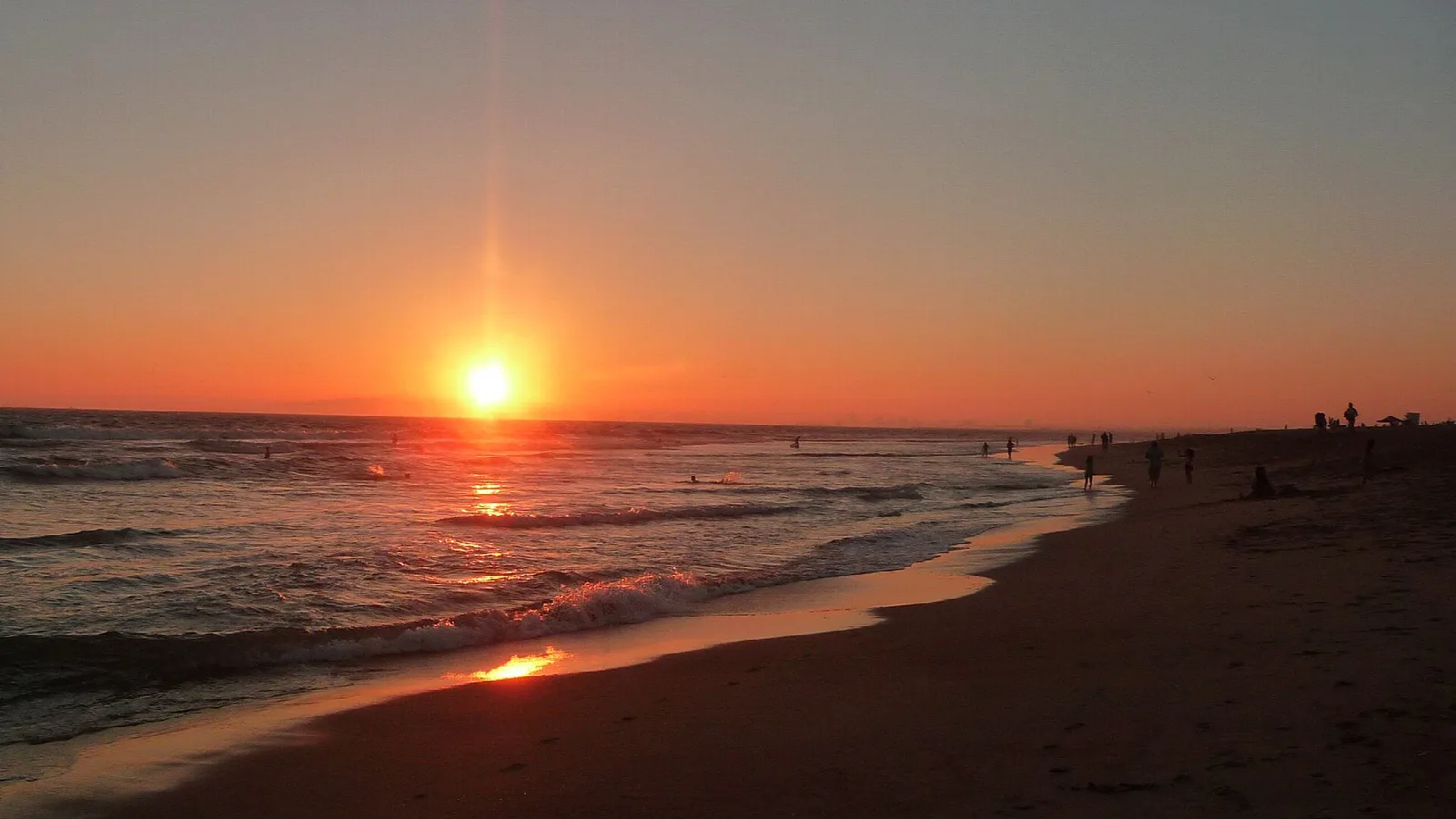 Sun setting over the ocean with a long dark beach