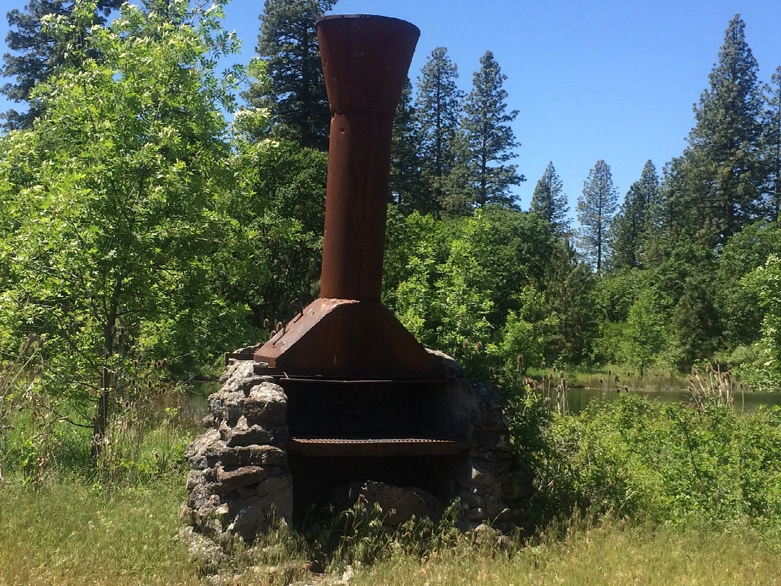 Rusty stove chimney on a stone base among green trees