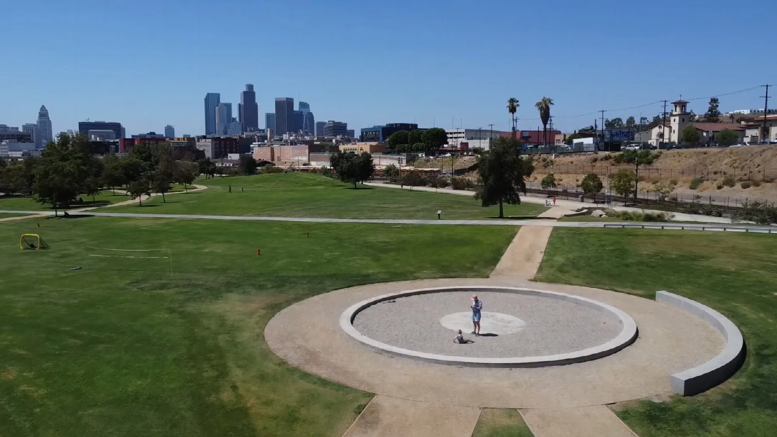 Aerial view of a green lawn with a circular plaza and downtown skyline