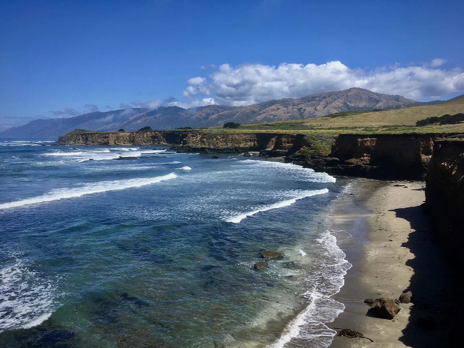 Blue ocean with waves along a bluff and mountains up the coast