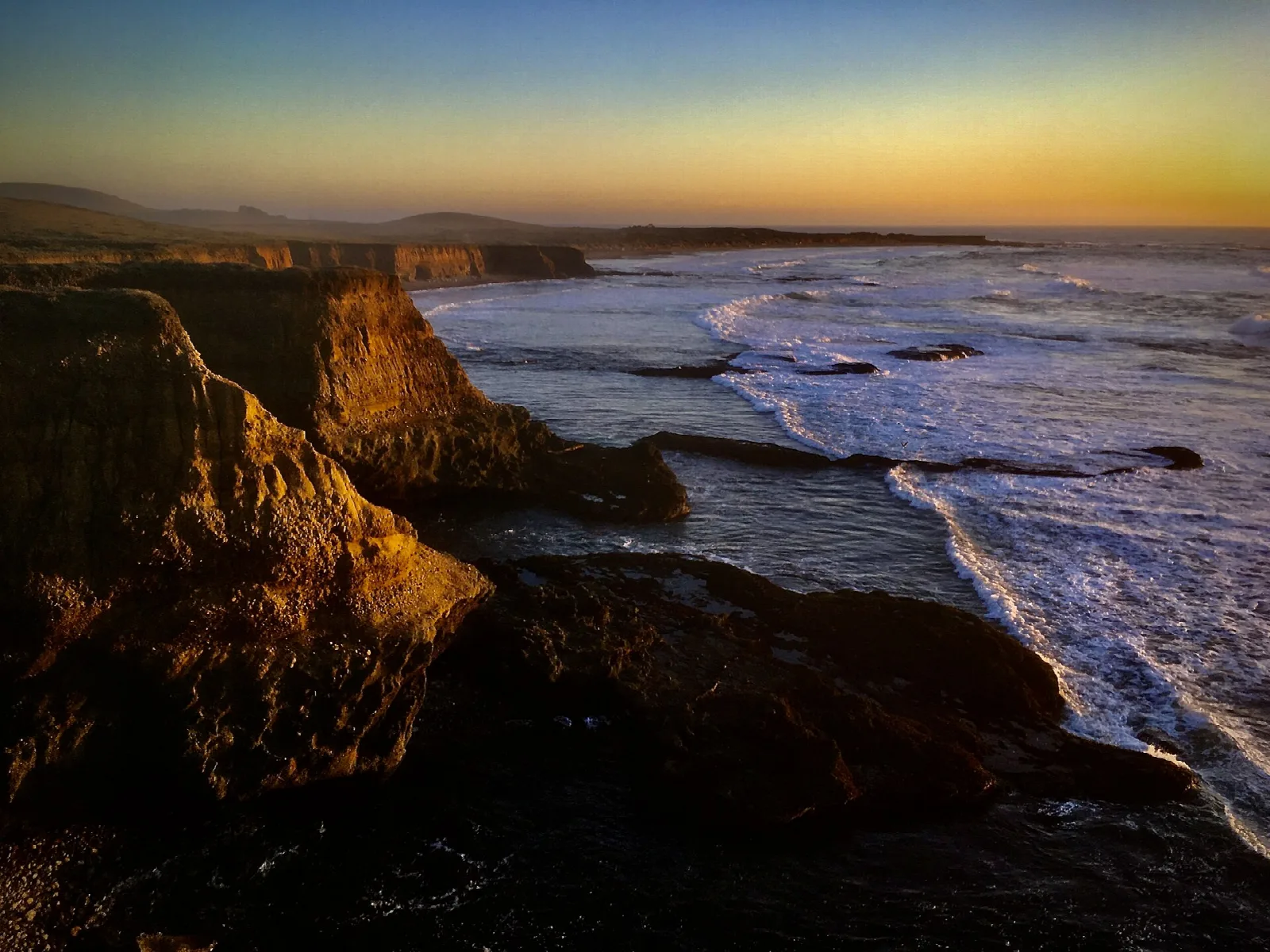 Rocky bluffs and surf lit by golden evening light