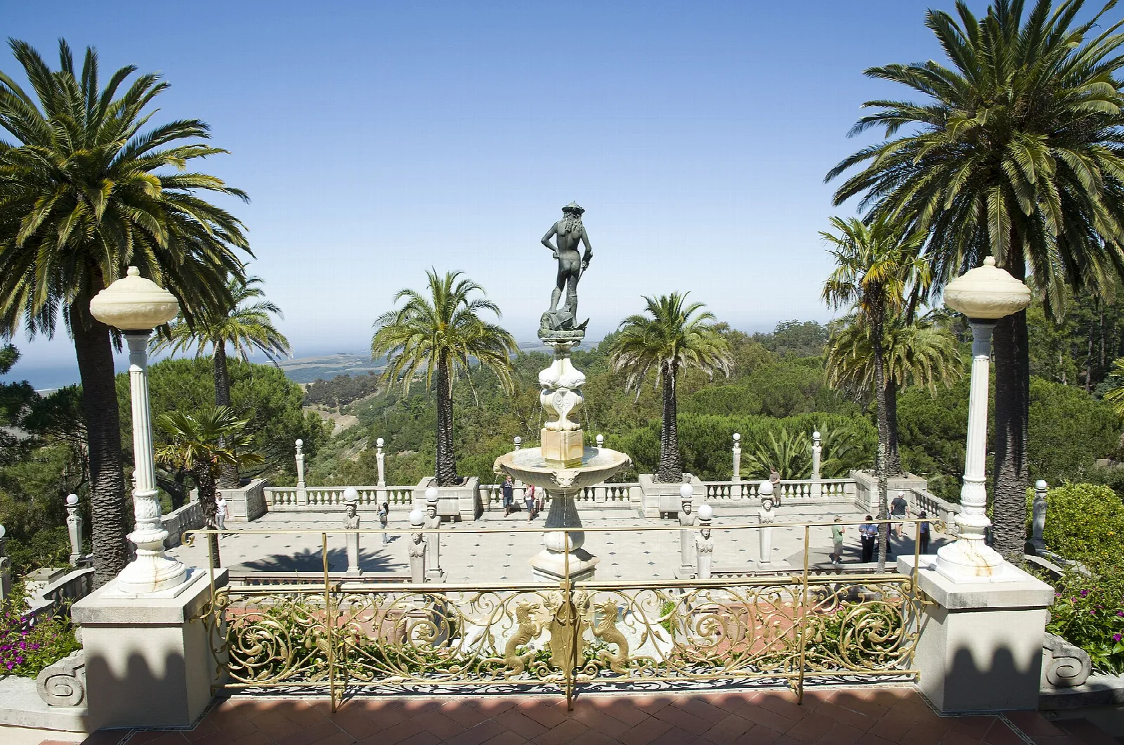 Terrace with a statue, palm trees and a fountain under blue sky