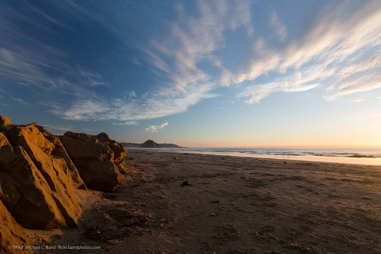 Orange cliffs and a beach under a sky streaked with clouds at sunset