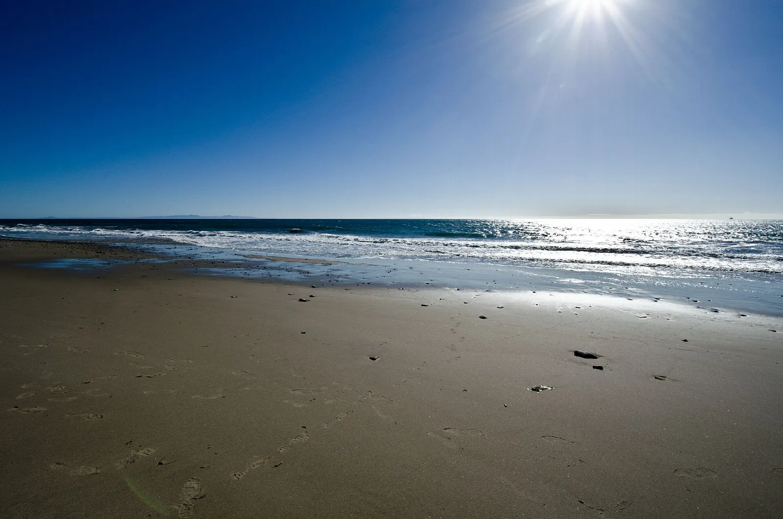 Sun flaring over a flat sandy beach and bright ocean