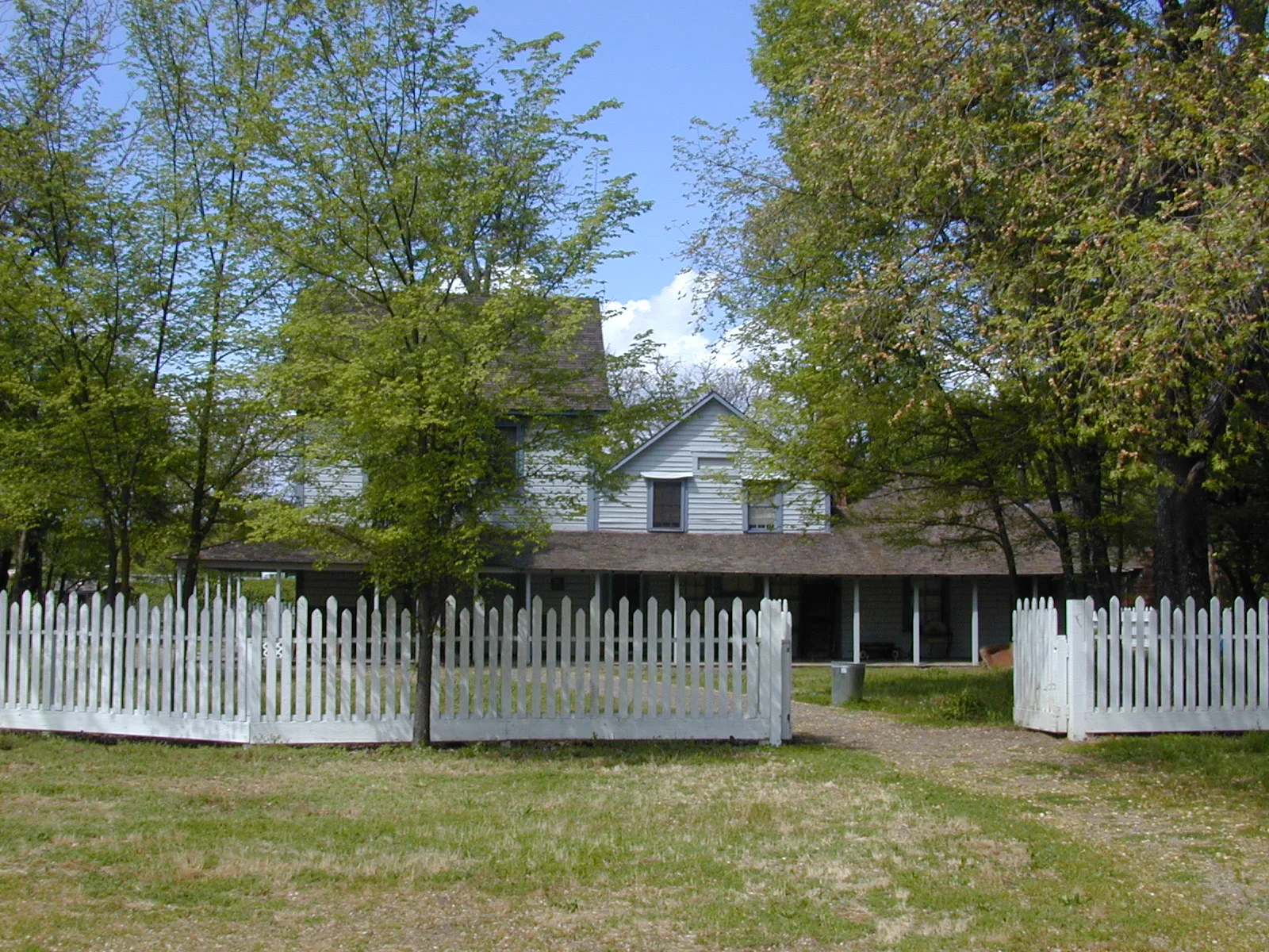 White ranch house with a porch behind a picket fence and green trees