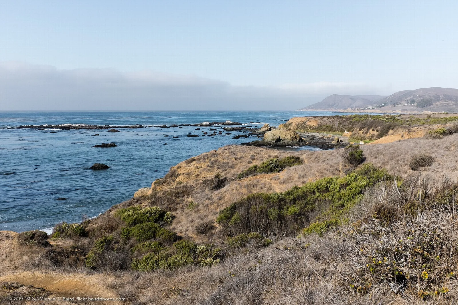 Grassy bluffs dropping to blue ocean with a headland beyond