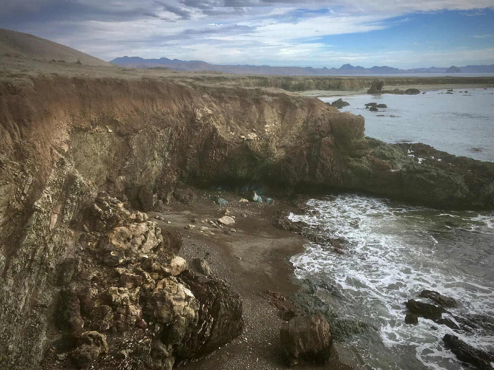 Eroded sandstone bluff above a cove with waves and a wide bay beyond