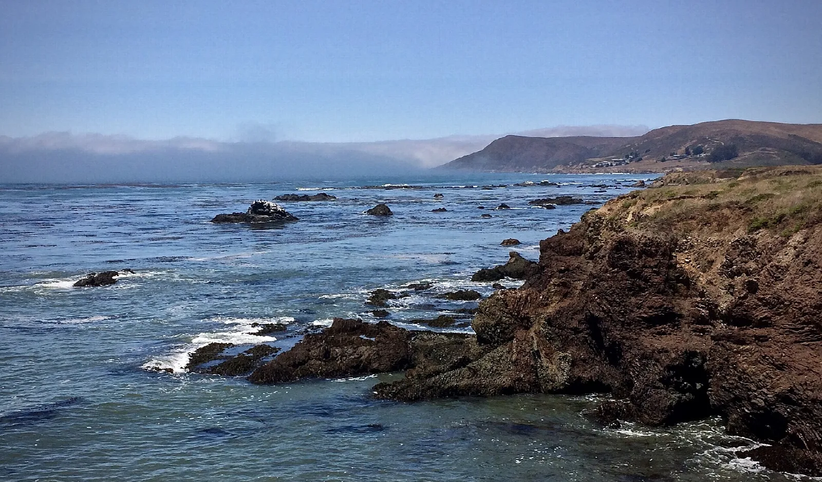 Rocky shore and ocean with fog bank and a ridge in the distance