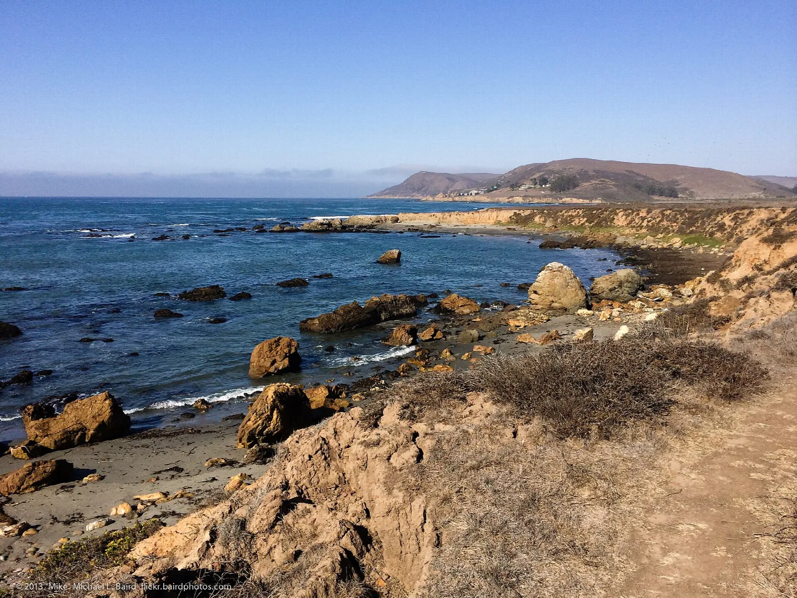 Rocky headland and blue ocean with a distant point under clear sky