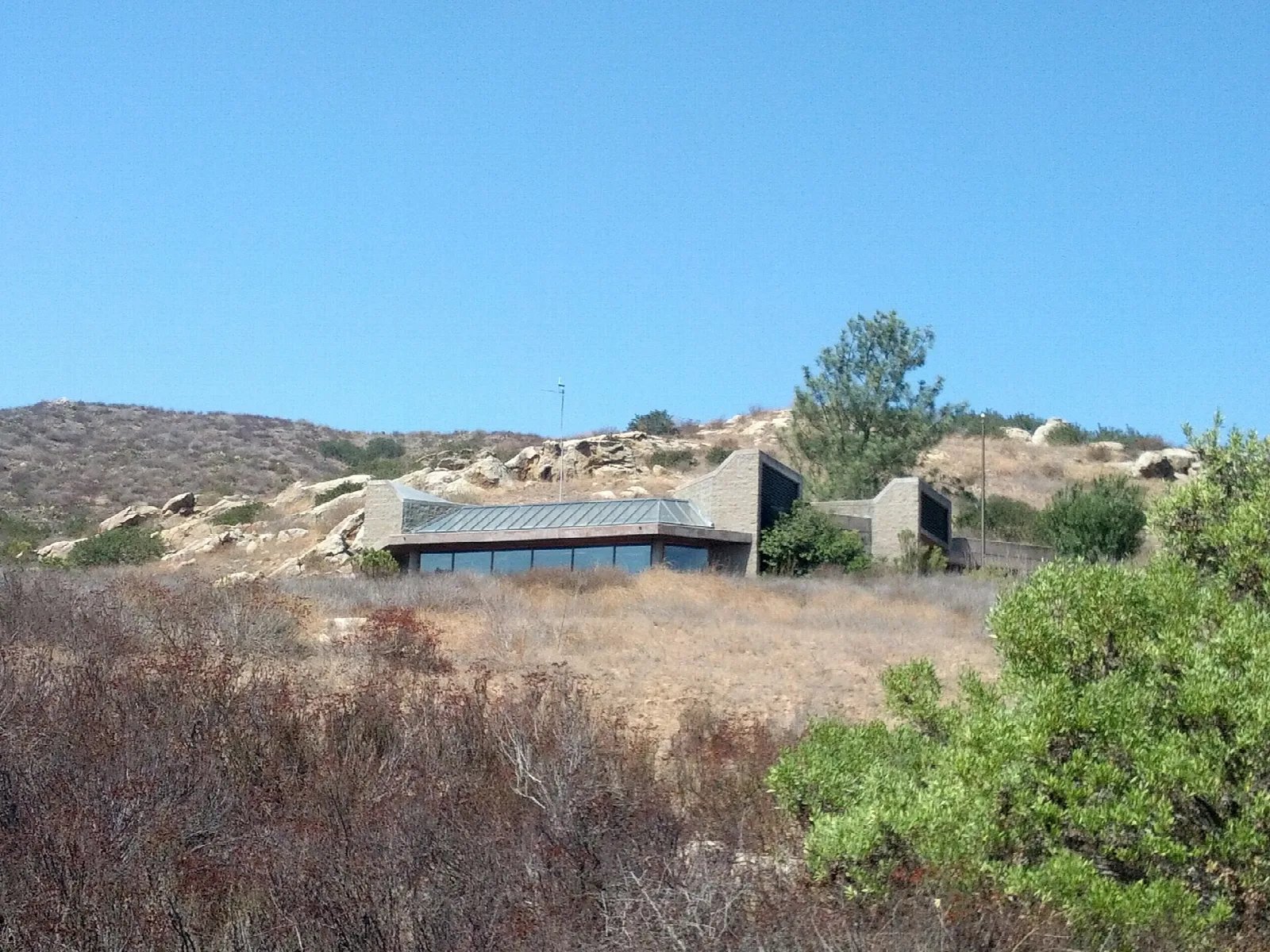 Low museum building on a dry hillside with shrubs and blue sky