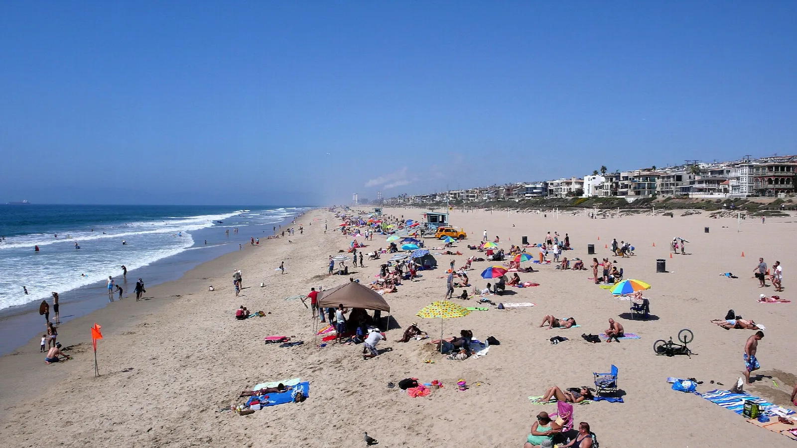 Crowded sandy beach with umbrellas and surf under blue sky