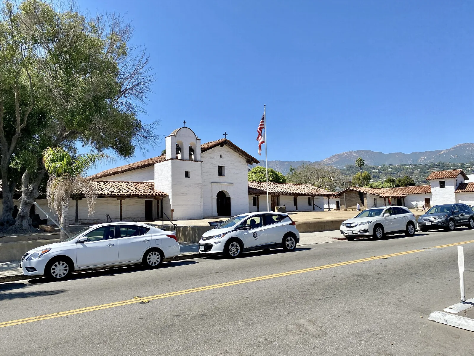 Street with parked cars and the white presidio chapel in the distance