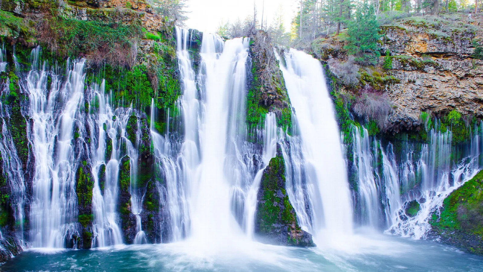 Tall waterfall splitting into streams above a blue pool