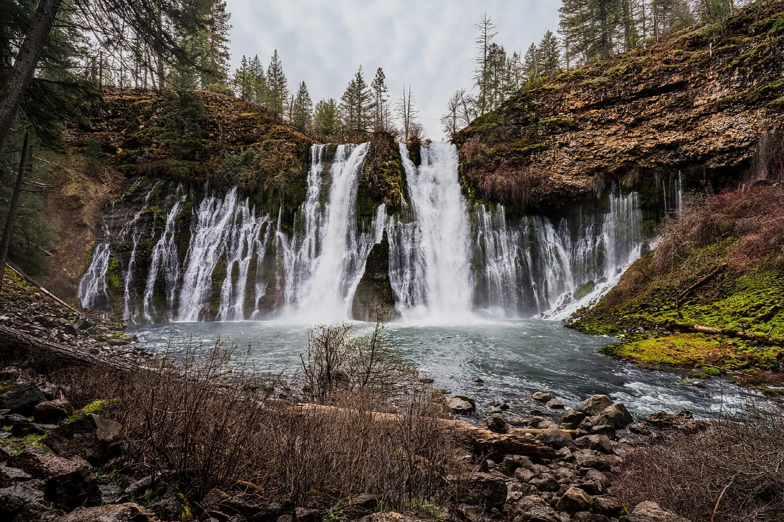 Wide curtain of waterfalls over a rock wall into a green pool