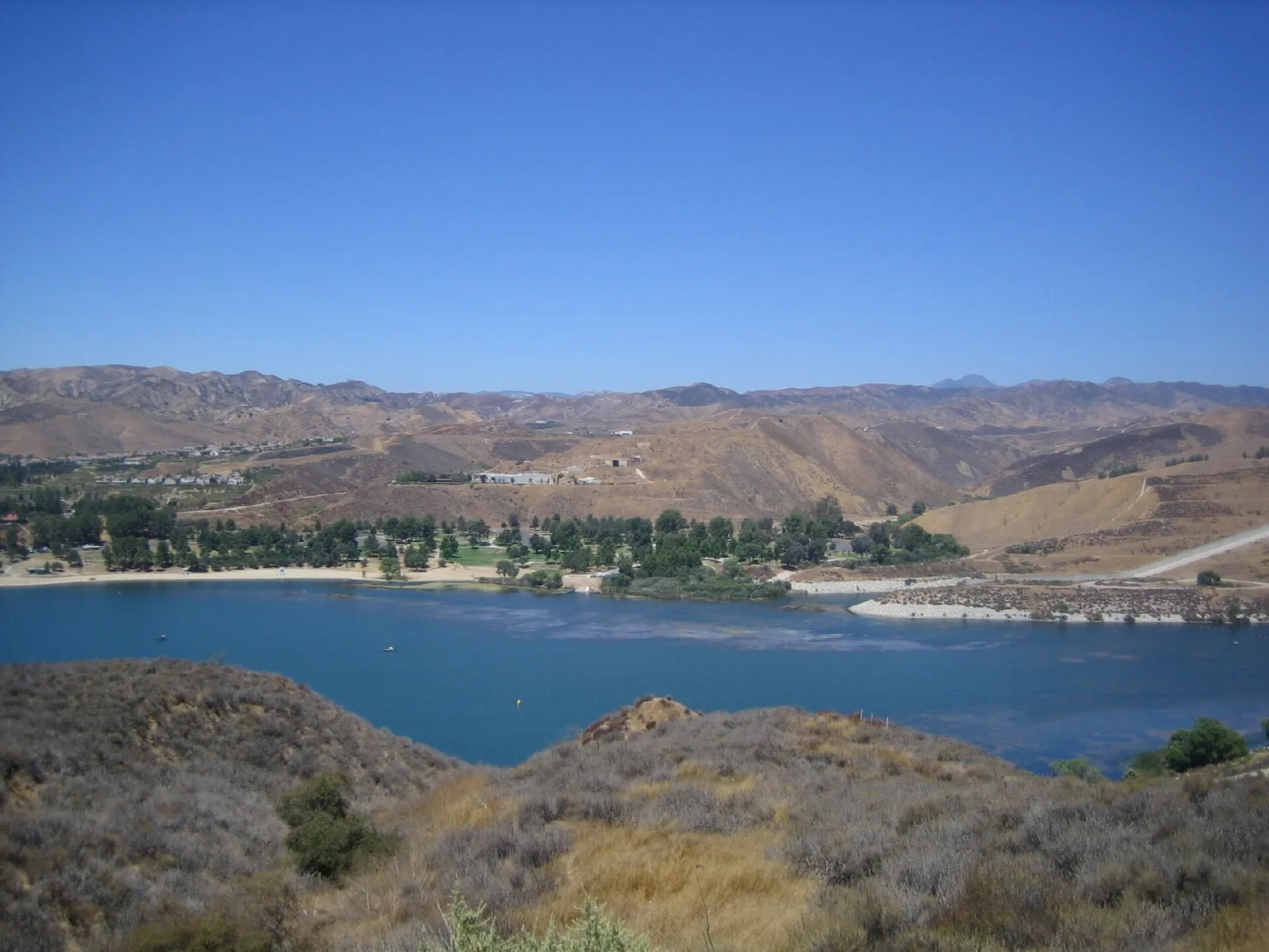 Blue lake with a shoreline of trees below dry brown hills