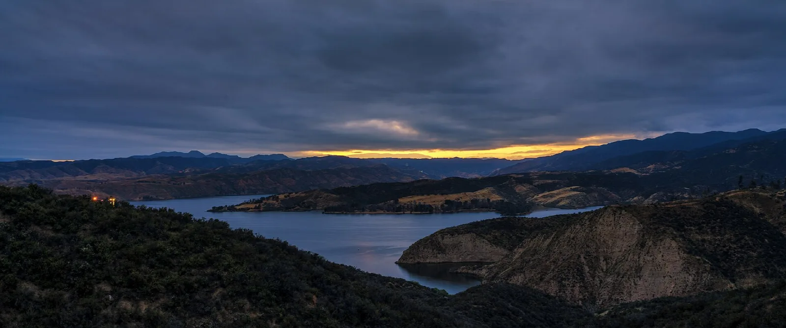 Lake and dark hills under storm clouds at dusk