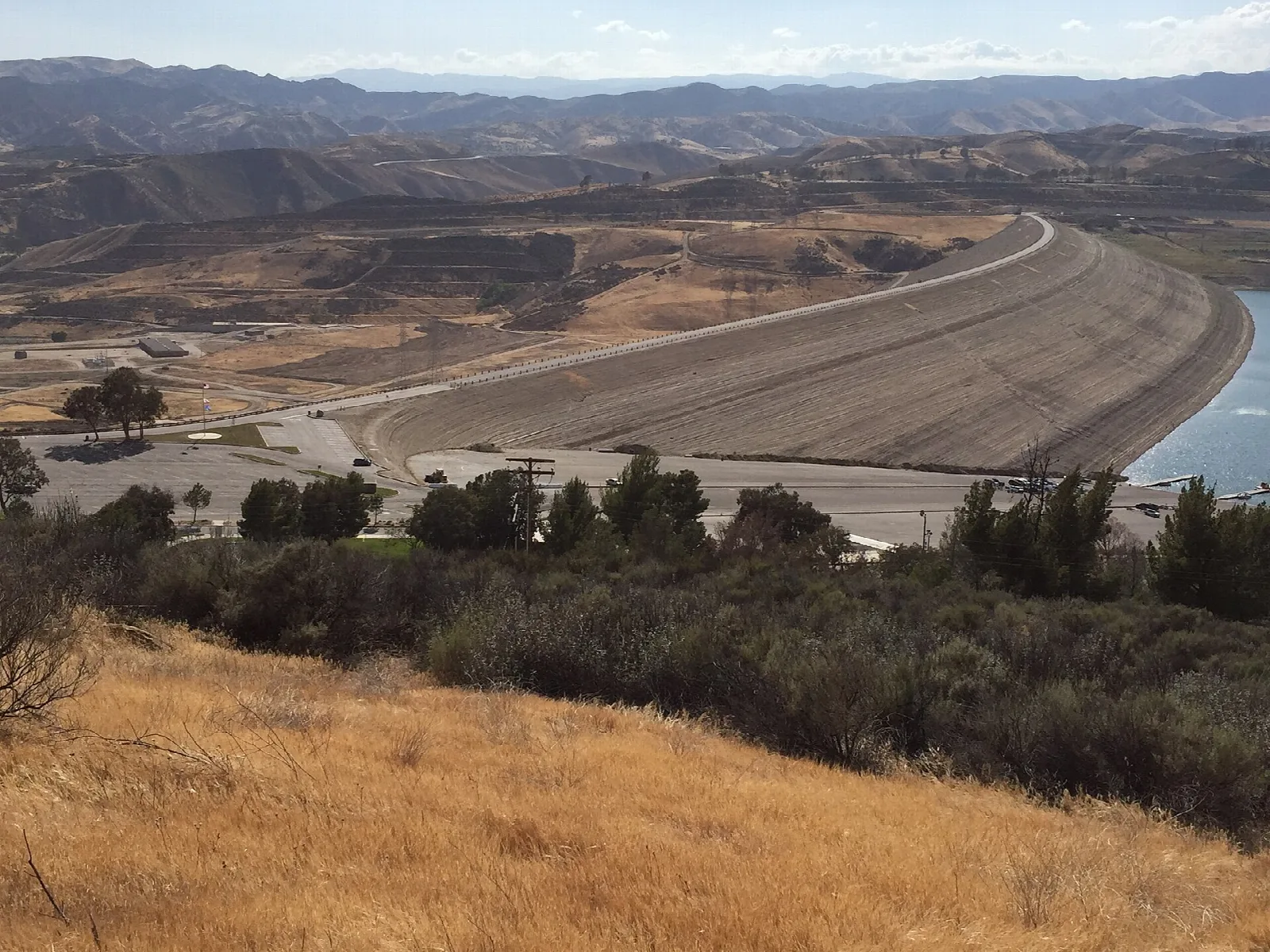 Long curved earth dam above a reservoir with dry hills around