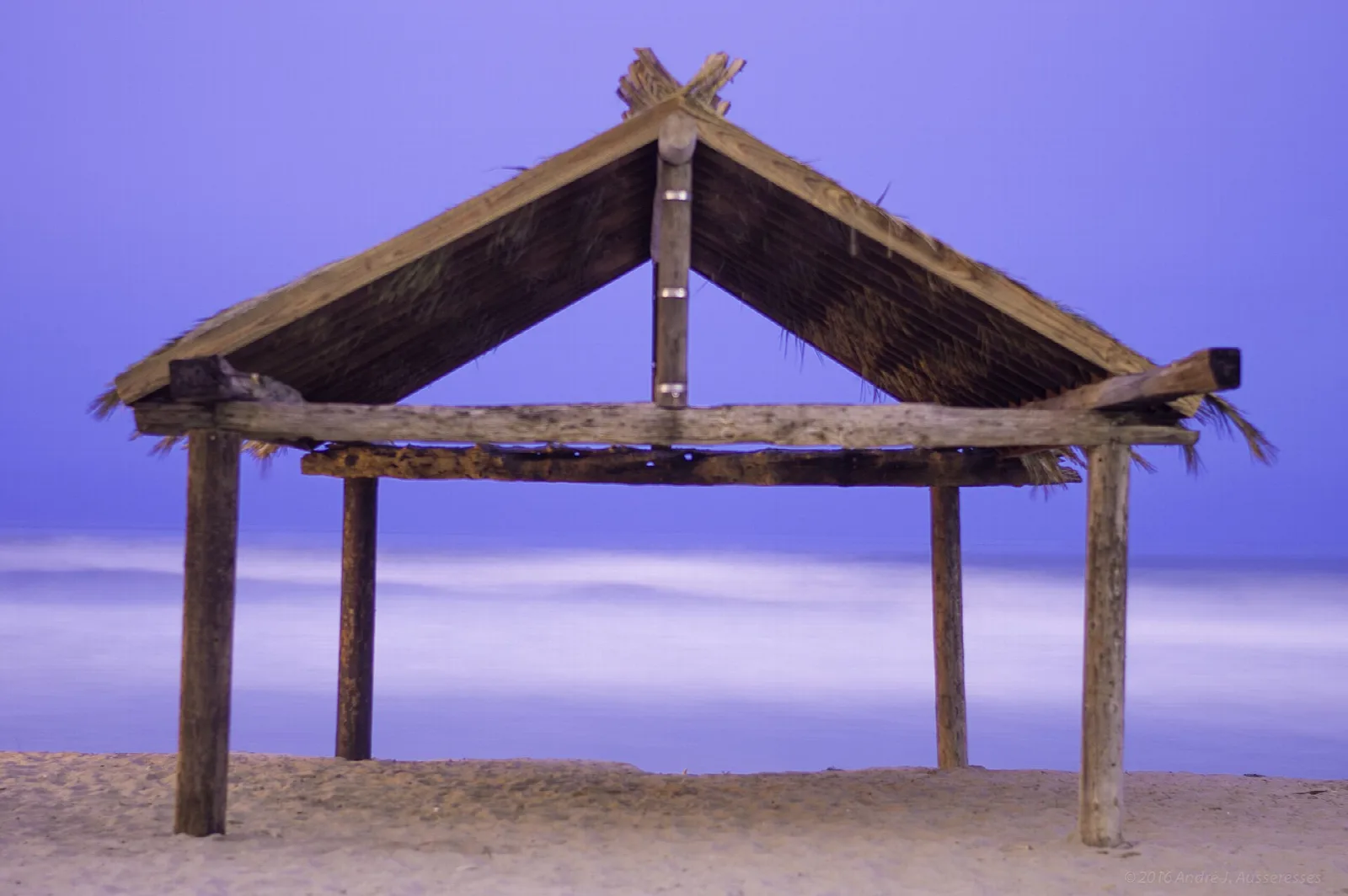 Weathered wooden palm hut on a sandy beach under a purple sky