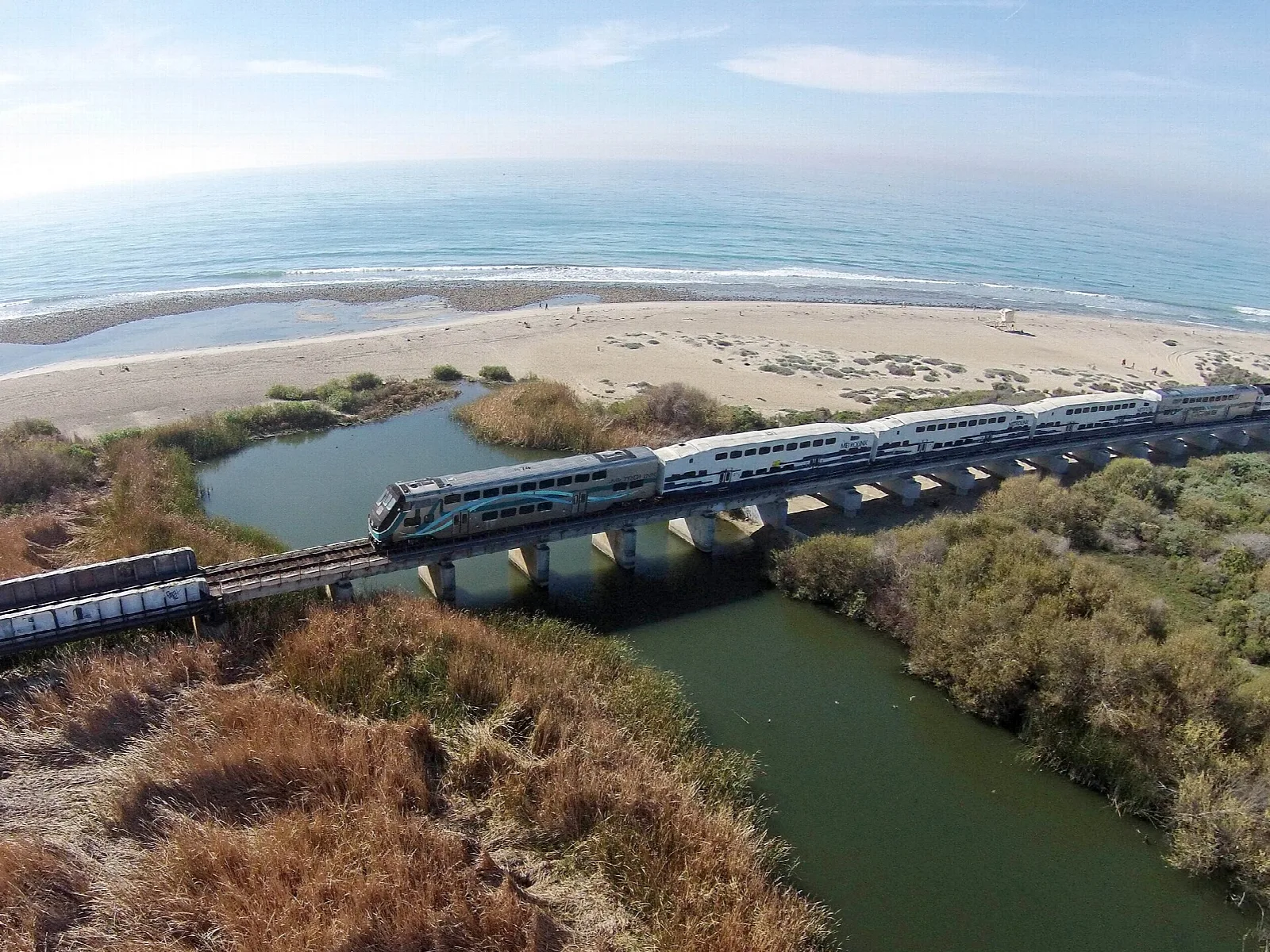 Train crossing a bridge over a creek mouth beside a wide sandy beach