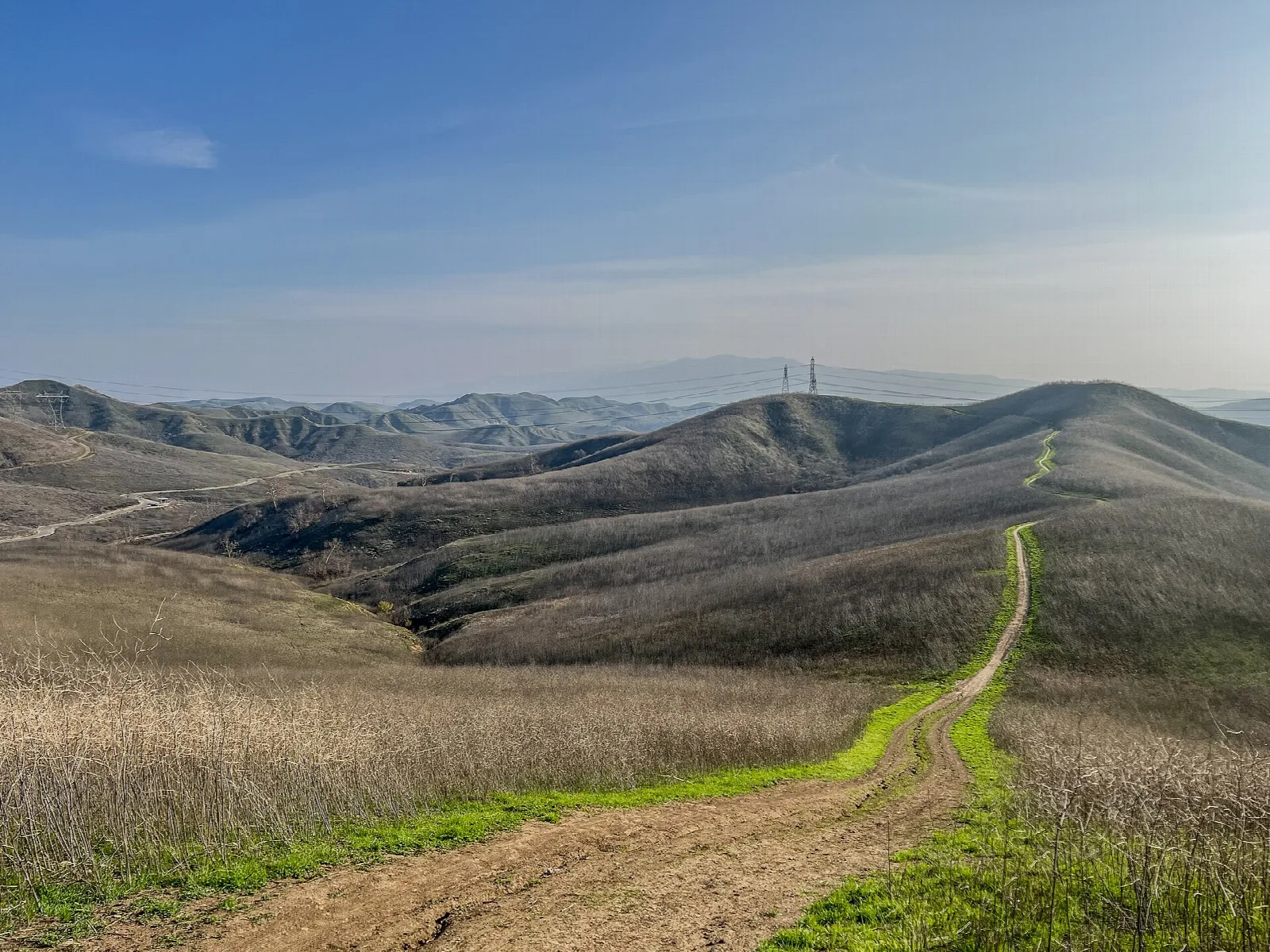 Dirt trail with green edges running over dry golden hills