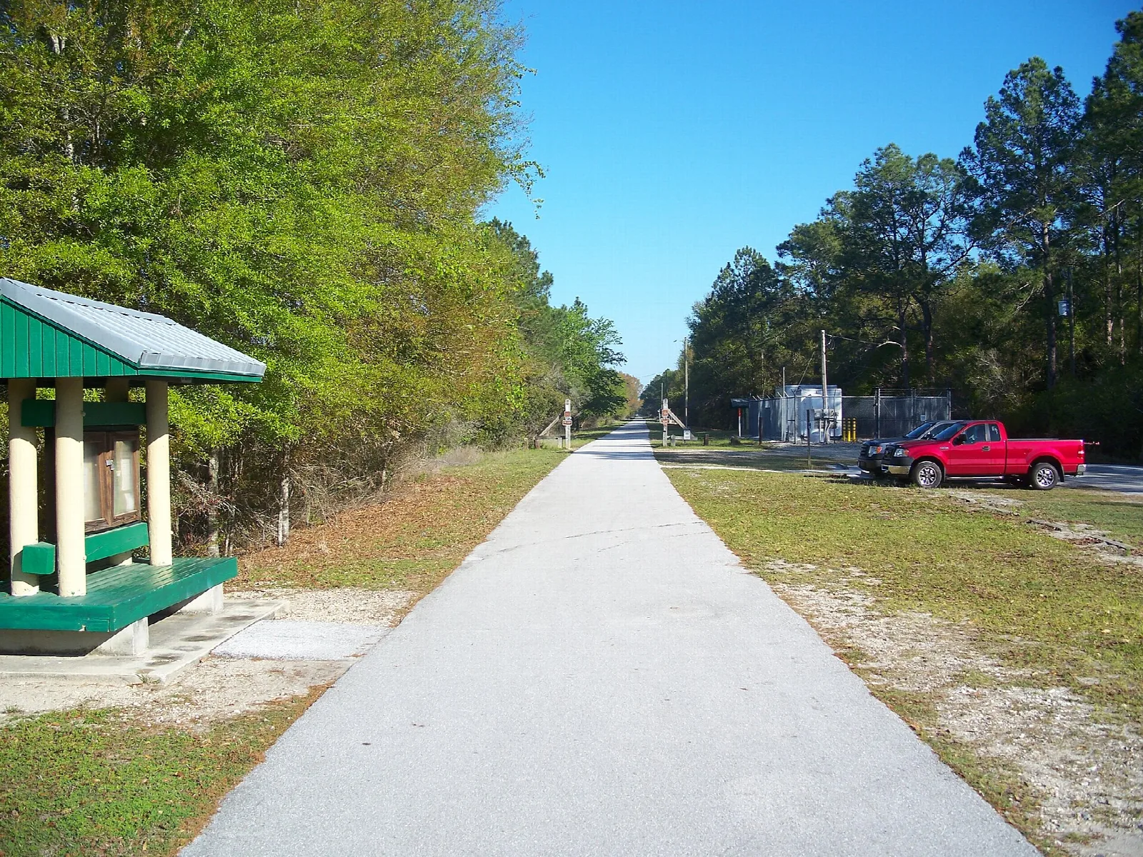 Paved trail beside a small shelter, with pines ahead