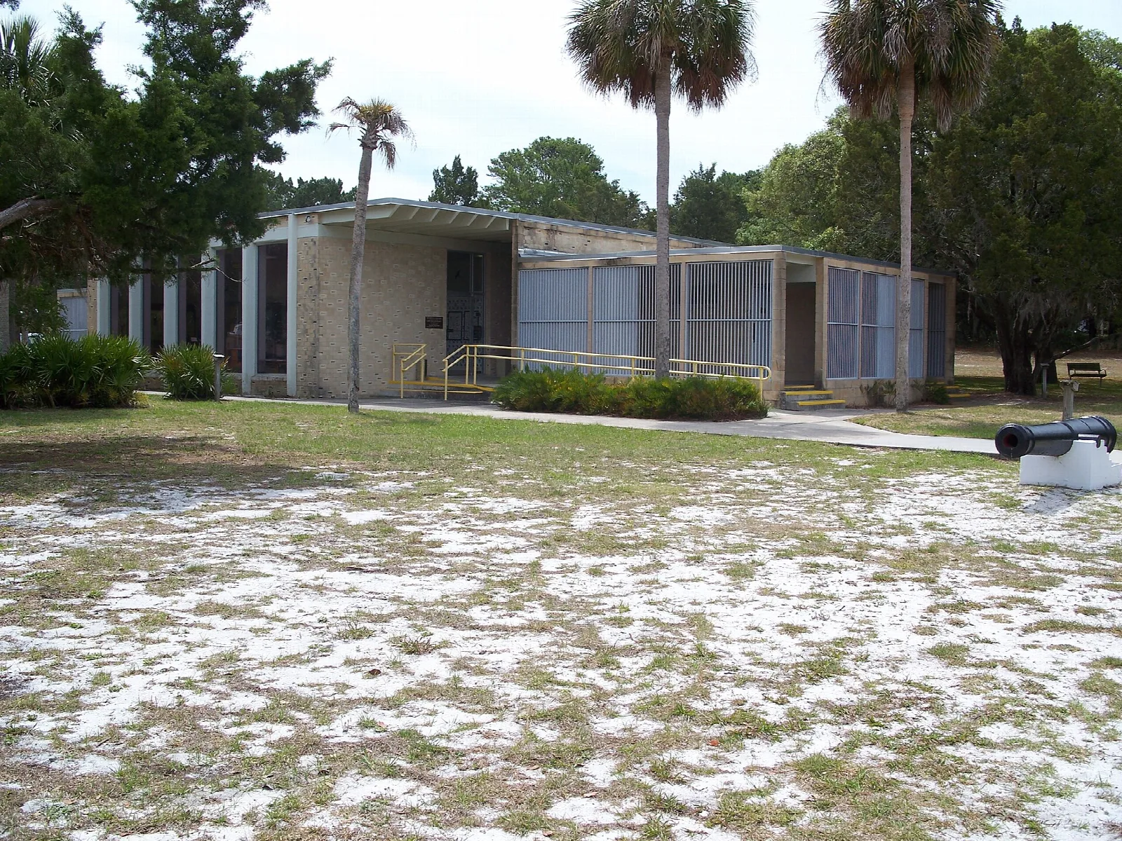 Low flat-roofed museum building with palms and a sandy lawn