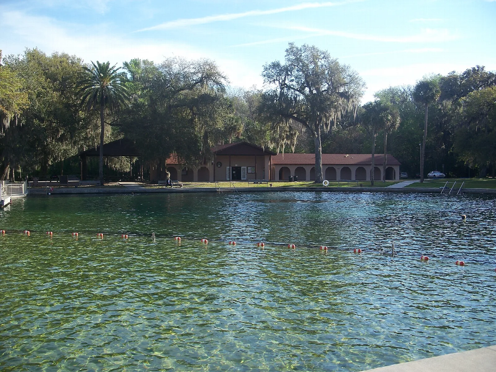Large clear spring swimming area with a tiled-roof building behind trees