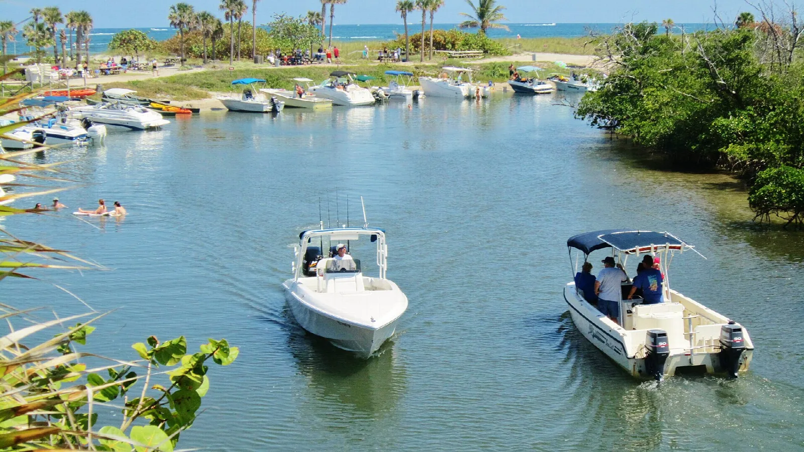 Two small boats crossing a lagoon toward a marina and palms