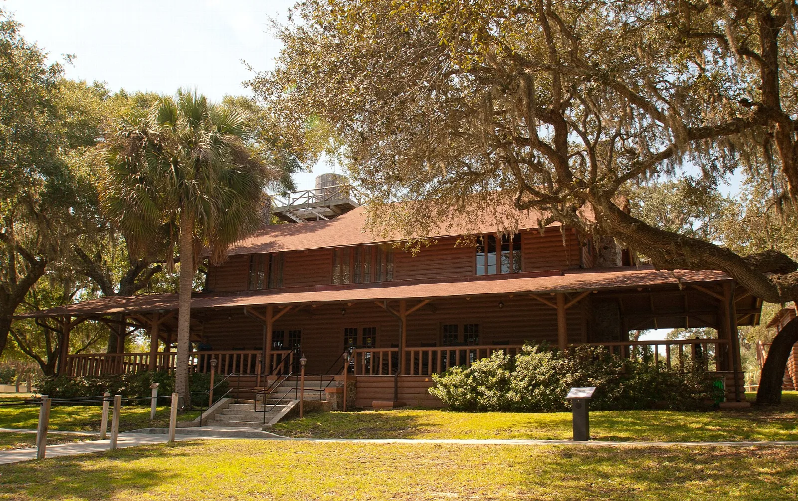 Two-story lodge with a porch among oaks and a palm