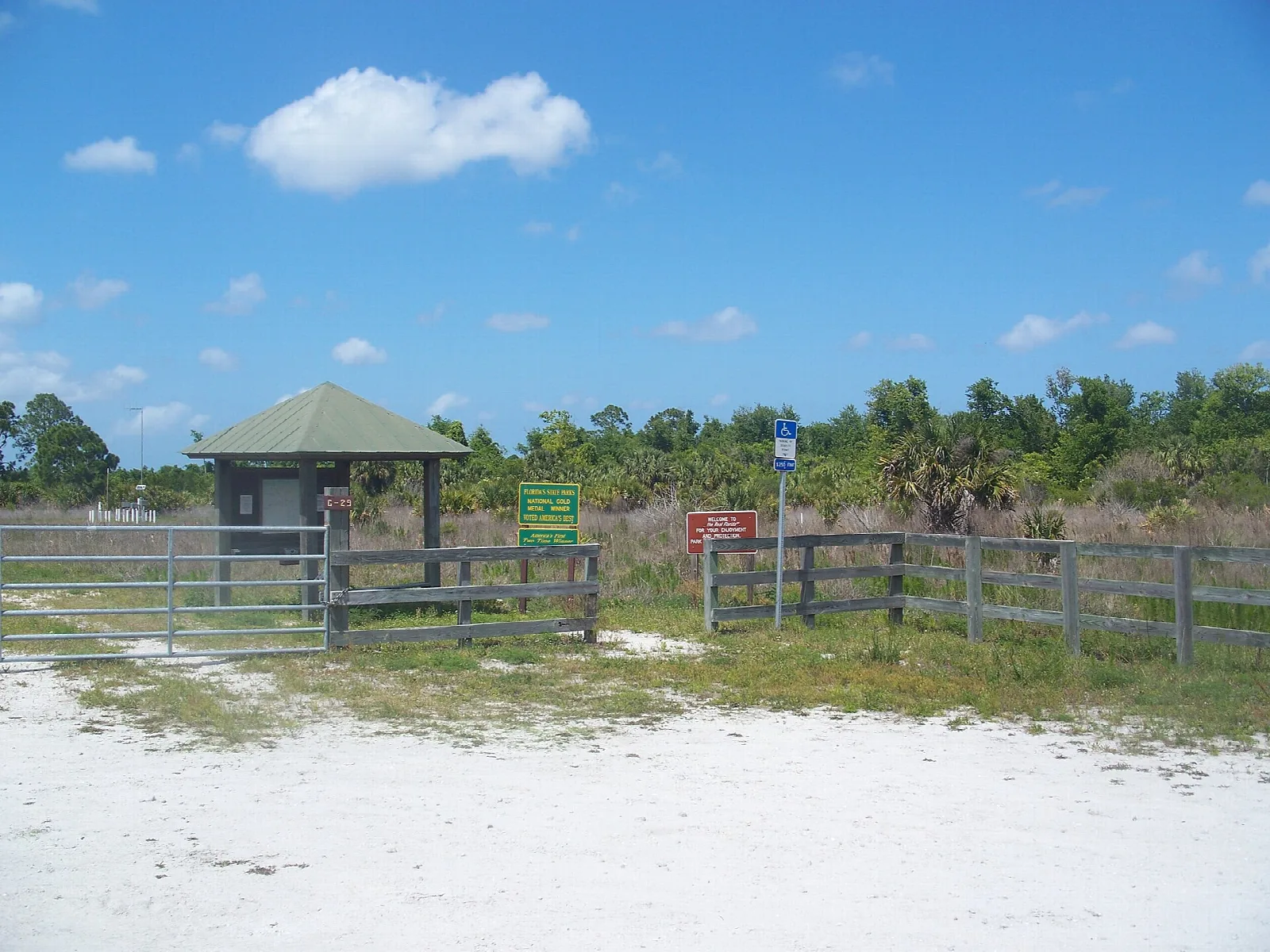 Sandy trailhead with a small shelter and fence in open flatwoods