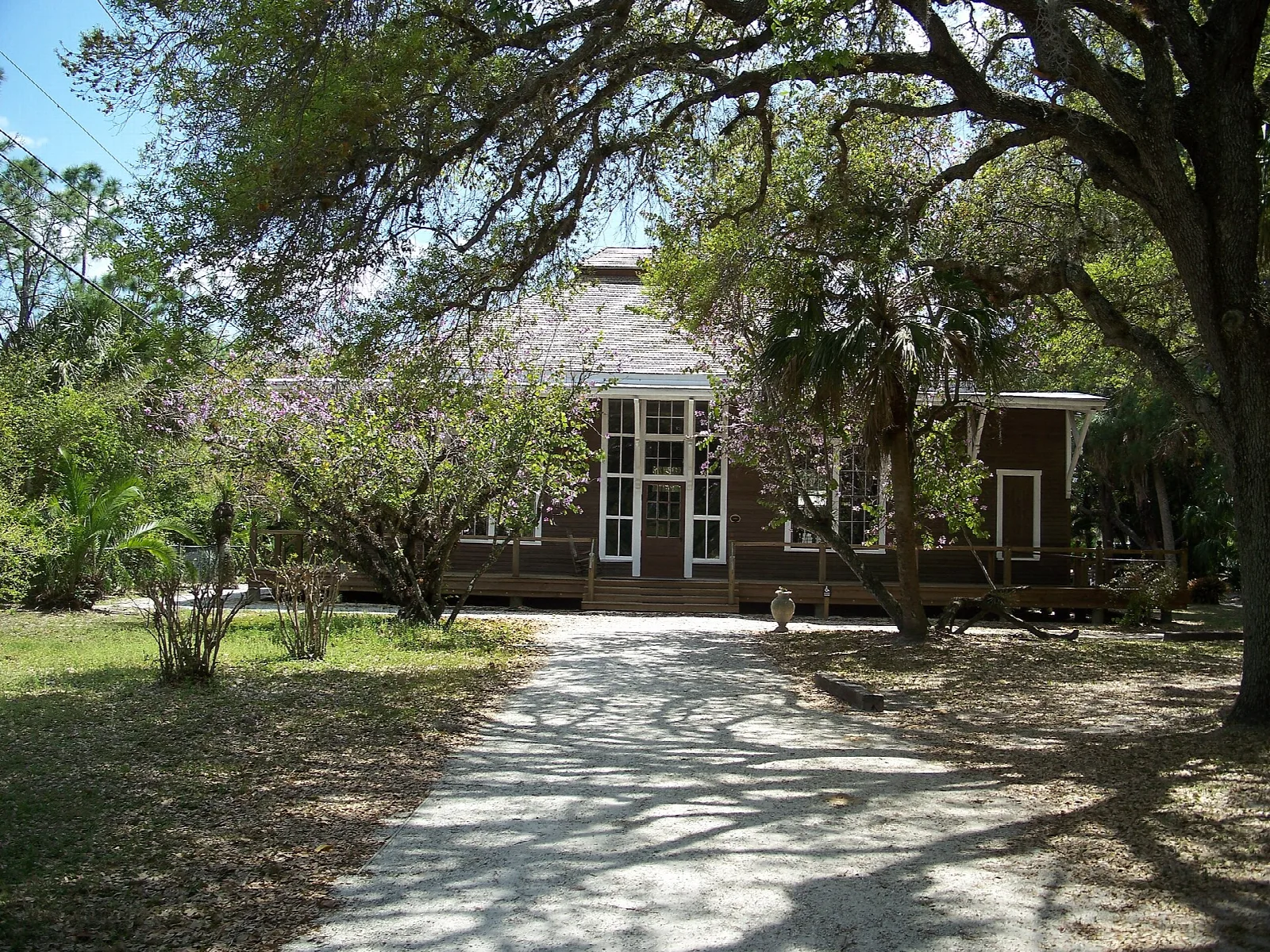 Wooden building seen along a sandy path under oaks