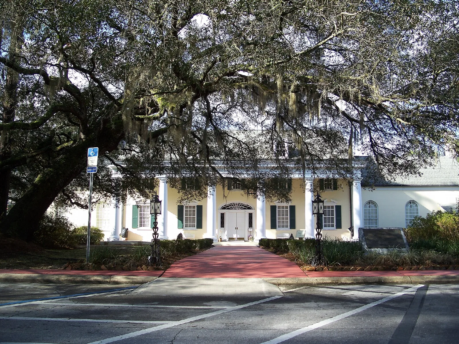 White columned building with a red brick walk under a big oak