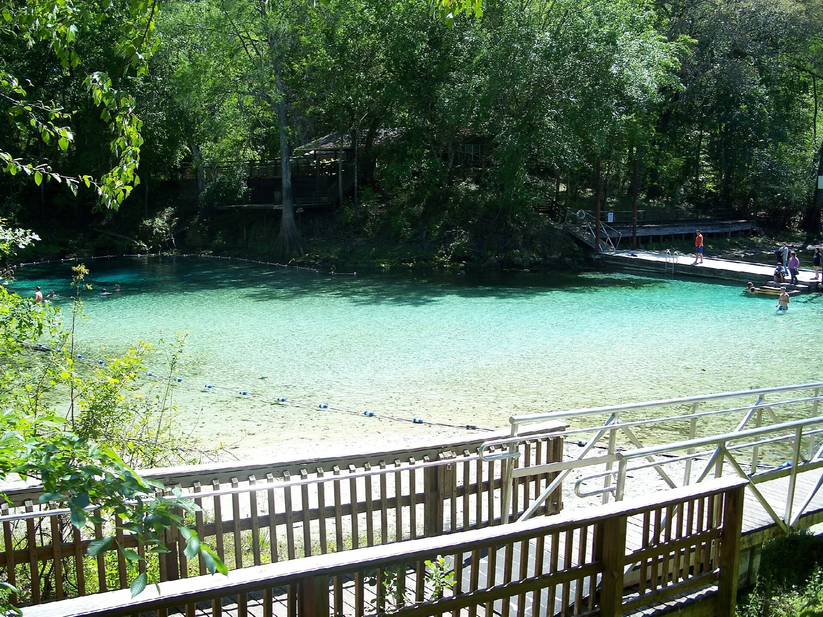 Pale turquoise swimming area with a wooden deck, ringed by trees