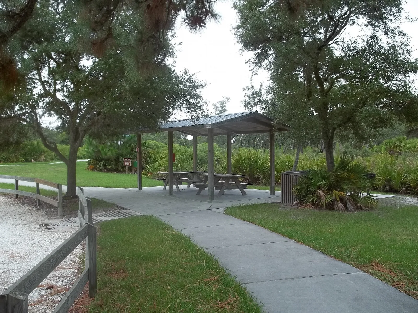 Picnic shelter beside a paved path and rail fence under oaks