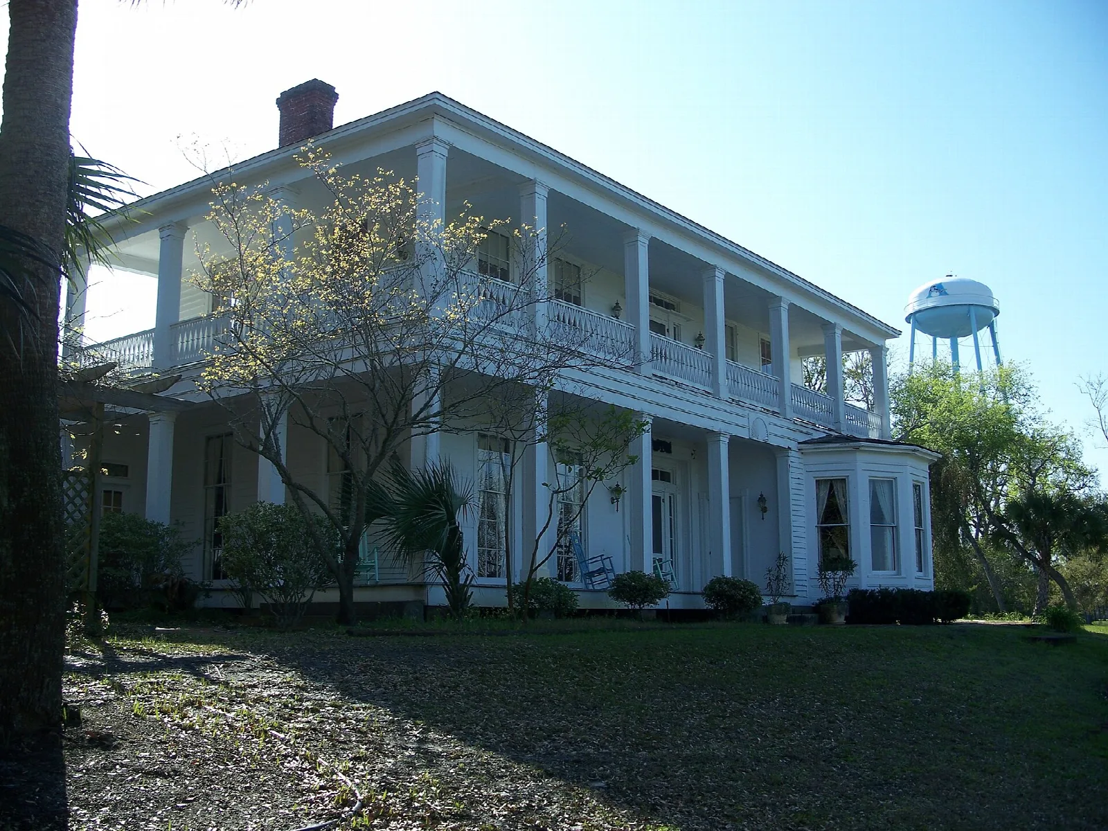 Large white house with balconies and a water tower behind