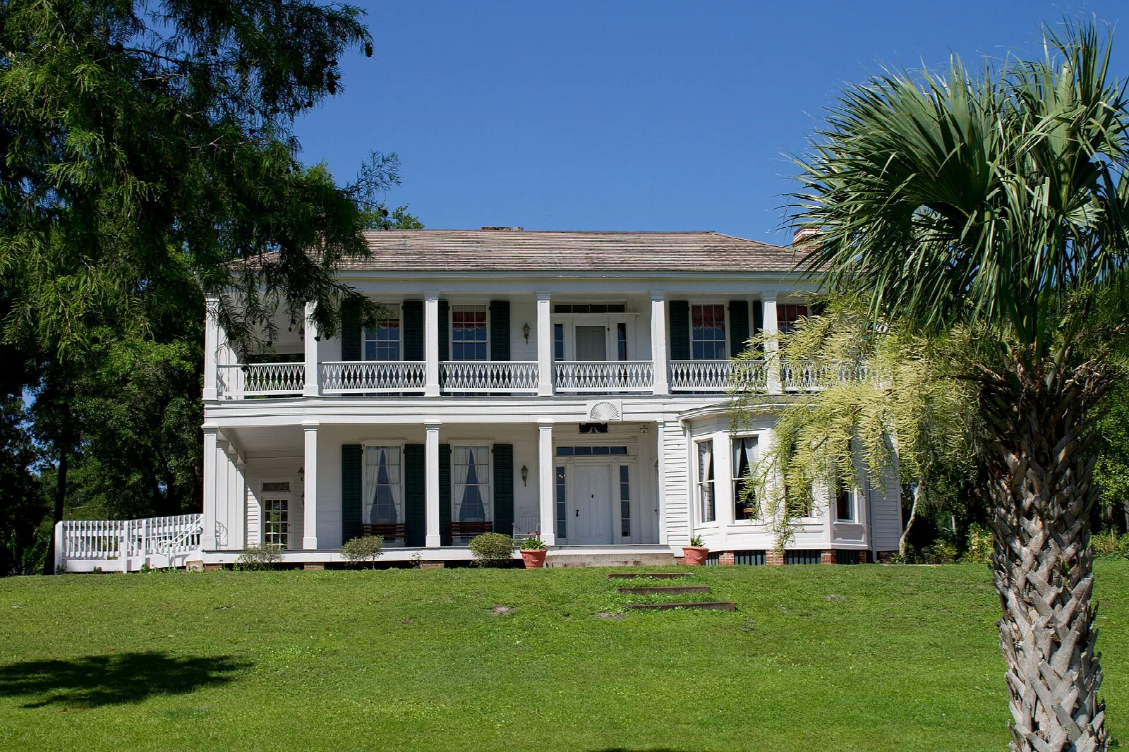 White two-story house with porches, a lawn and a palm
