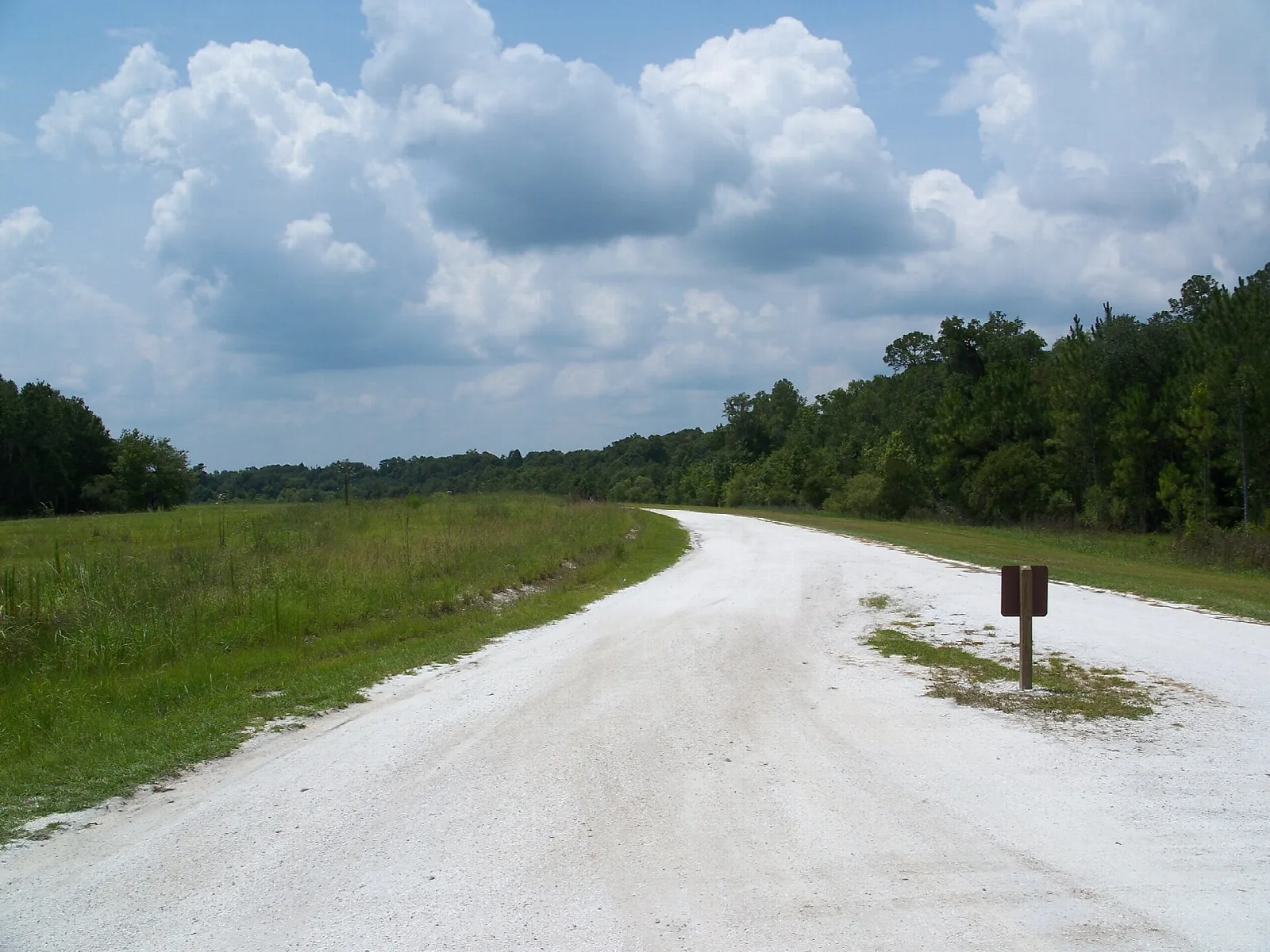 White sand road curving across open grass under big clouds