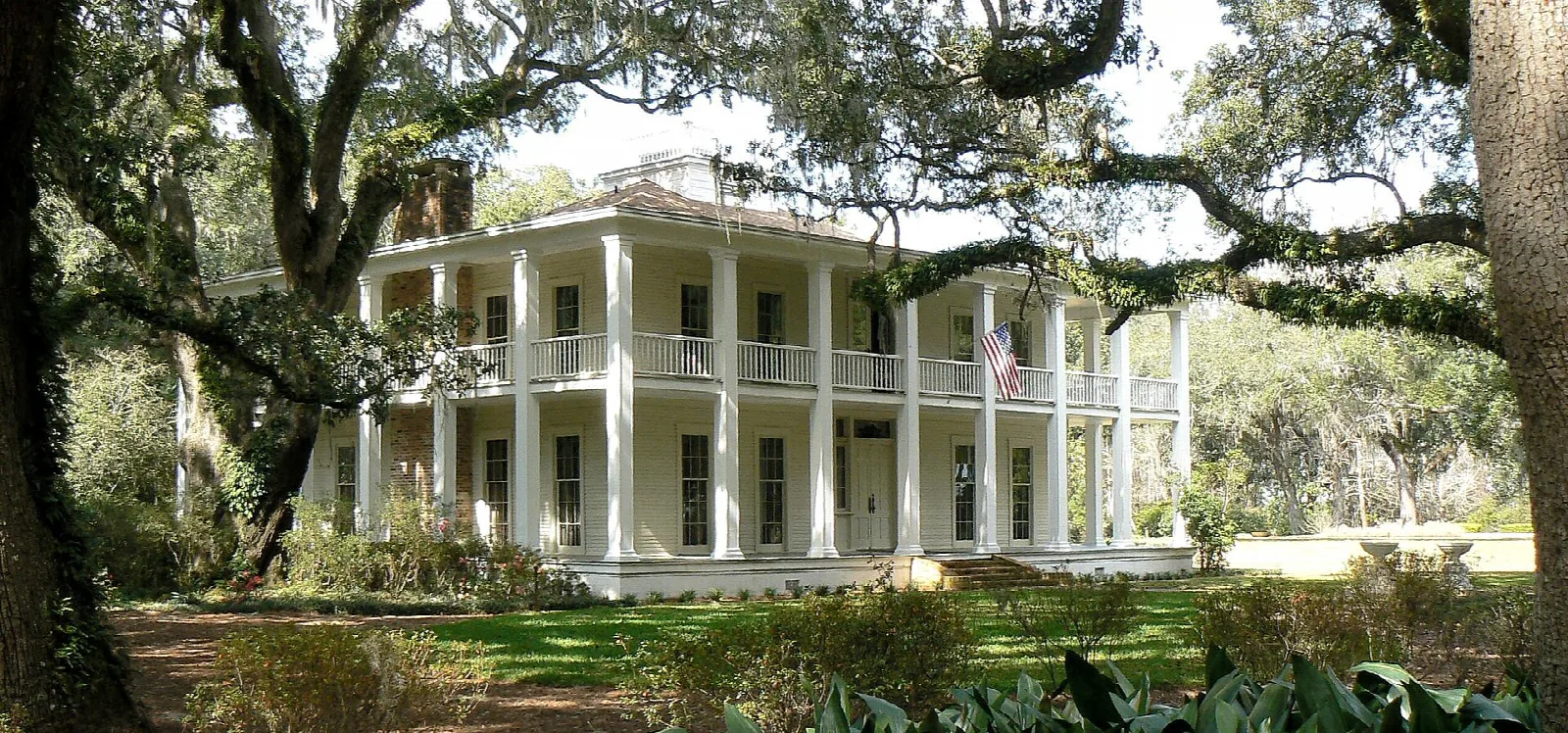 White columned house under oaks behind a green lawn