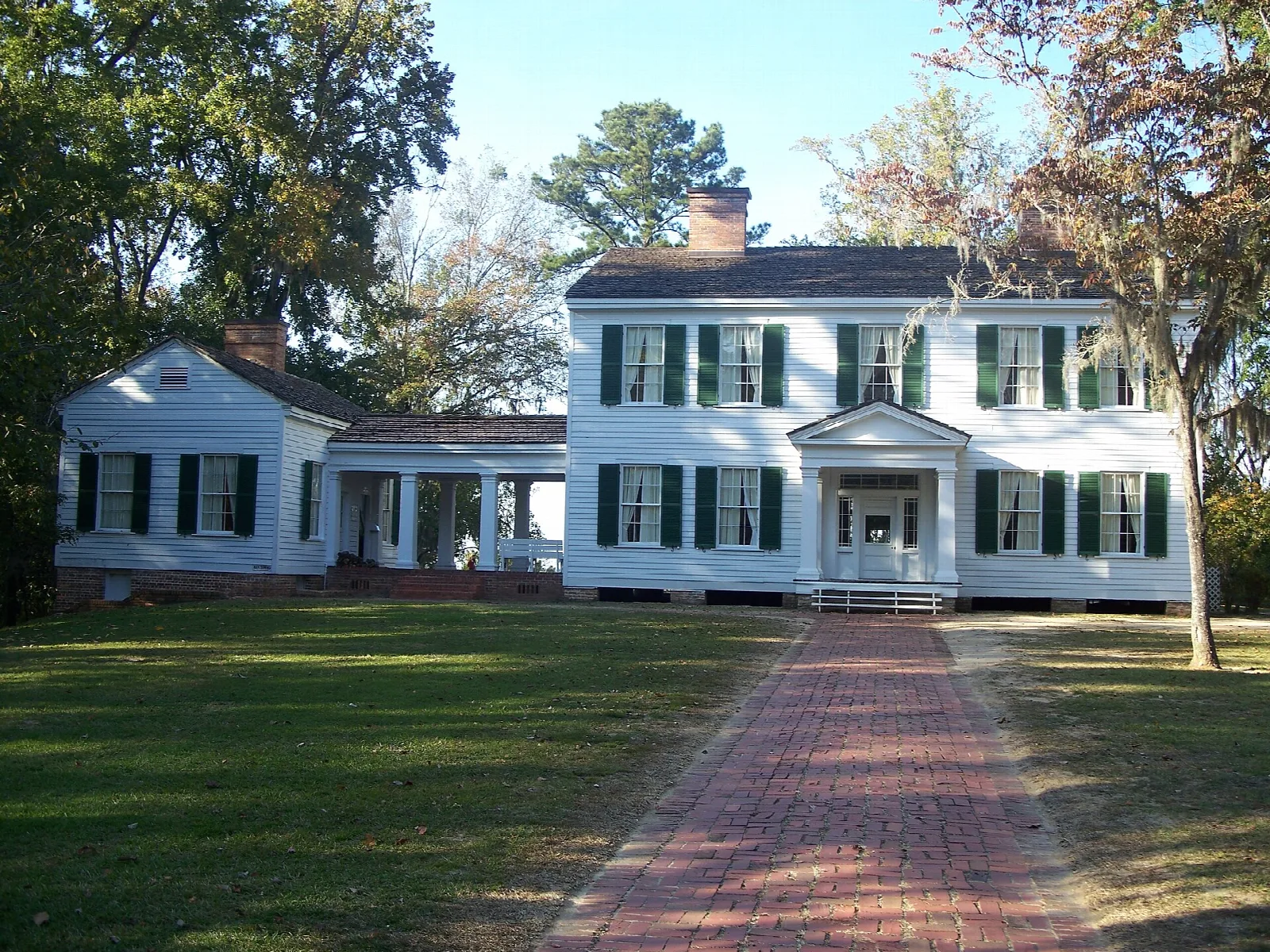 White two-story house with green shutters and a brick walk