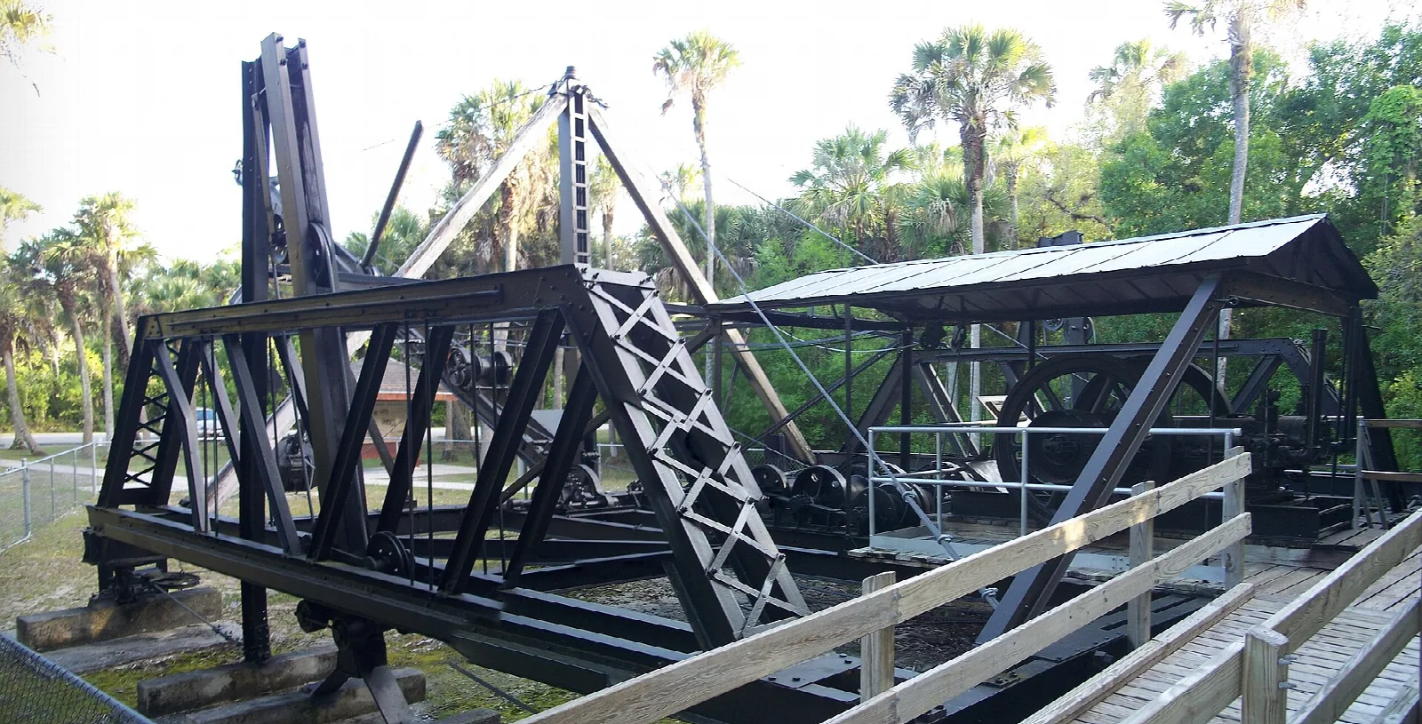 Black steel truss walking dredge on a platform with palms behind