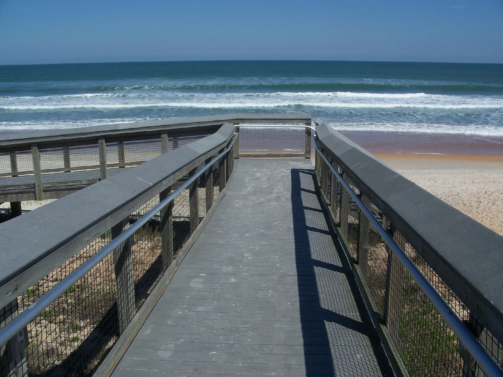 Boardwalk with railings leading to a surf-lined beach