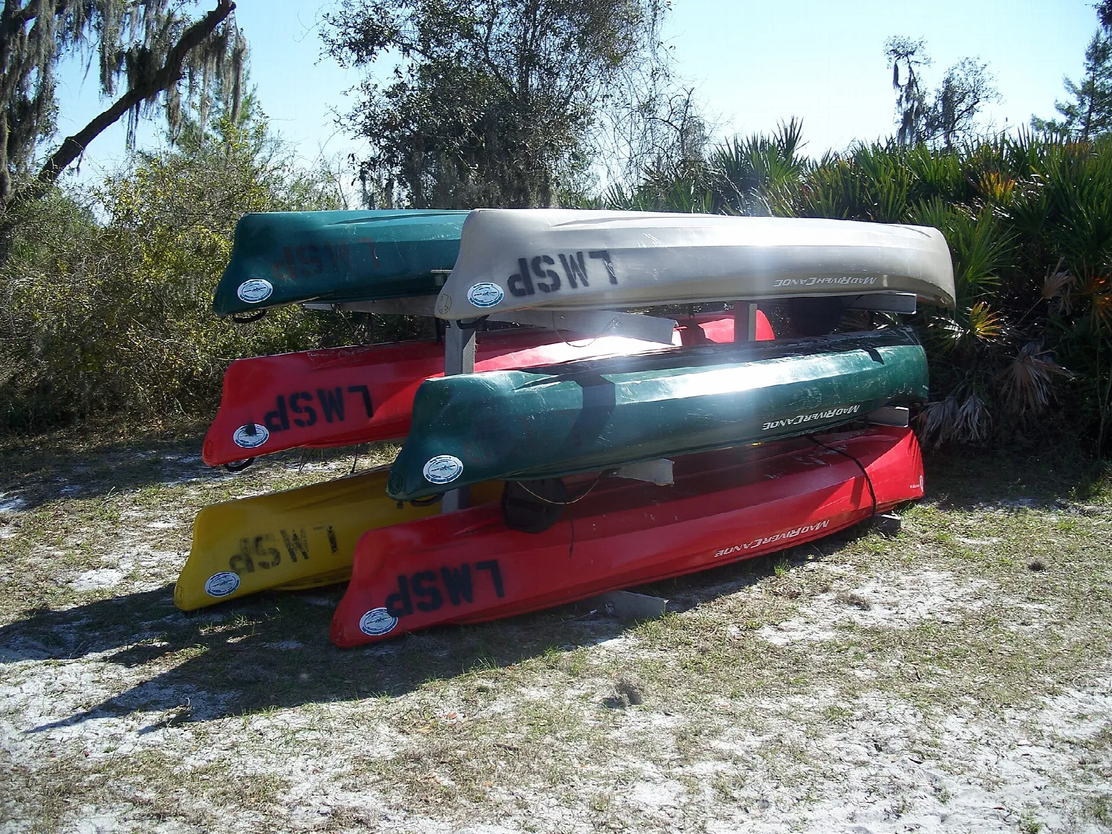 Stack of colorful canoes on sand under pines