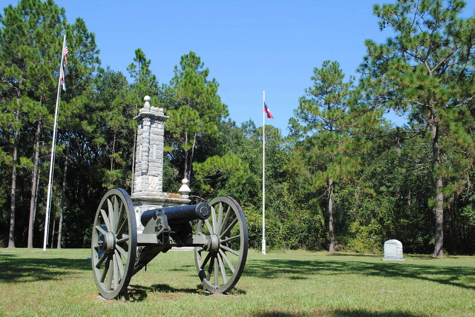 Cannon and stone monument on an open lawn among tall pines