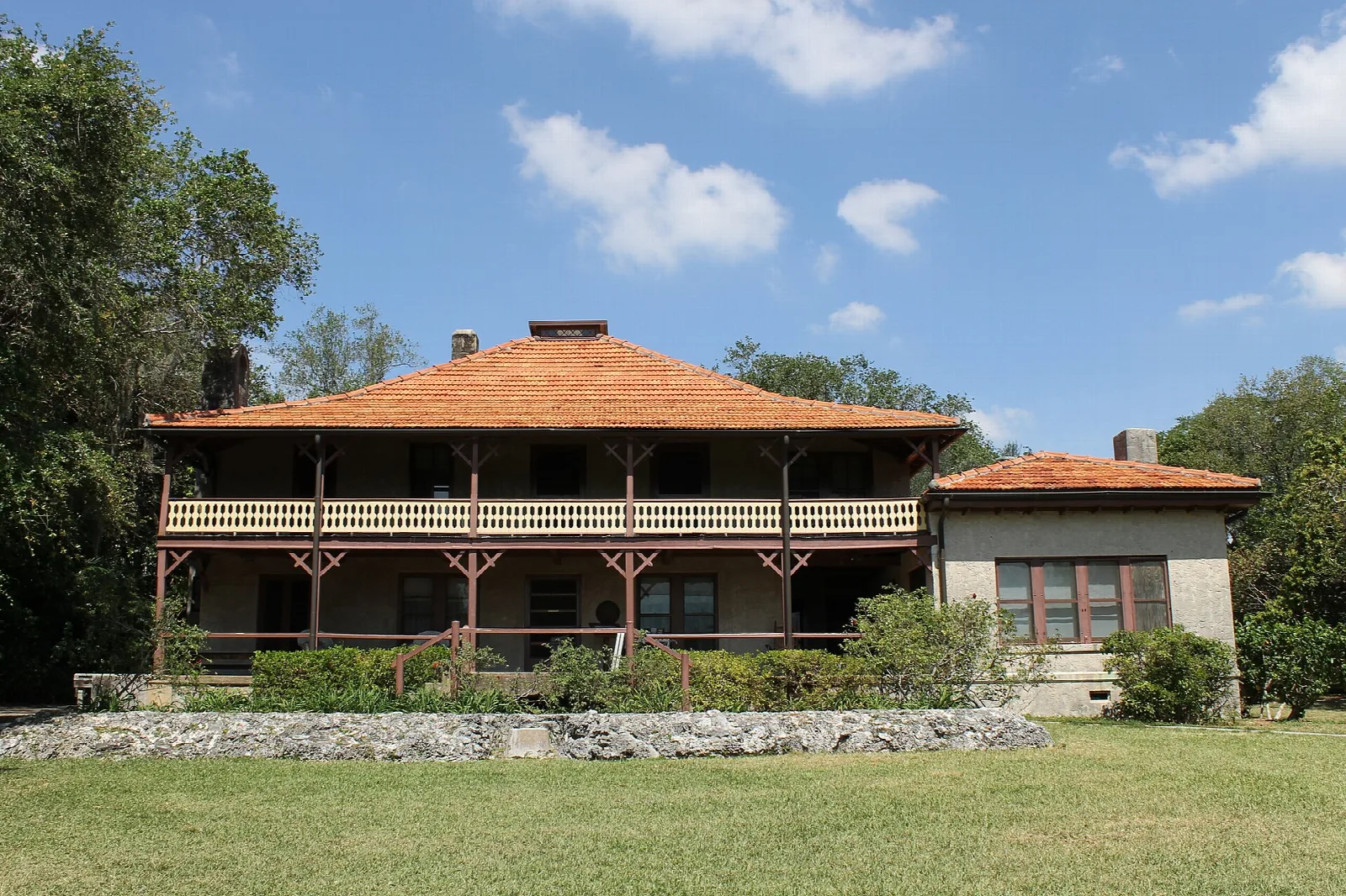 Two-story house with a red tile roof seen across a green lawn