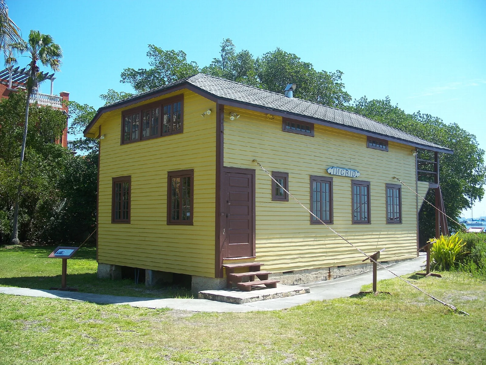 Yellow two-story wooden building with a gray roof and palms